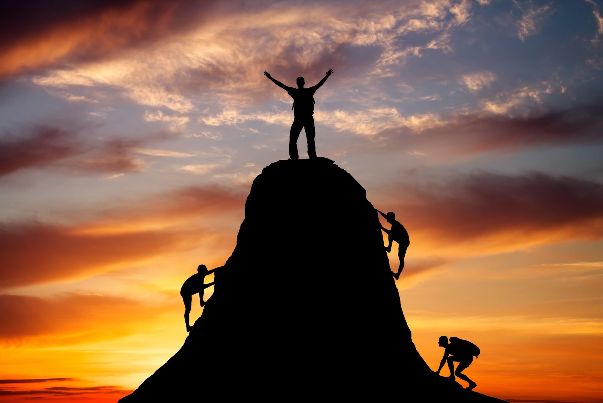 Man on top of the mountain and the other people to climb up on fiery orange background. Rock climber at sunset background. Sport and active life.