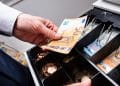Una persona sostiene euros en efectivo sobre caja registradosra.