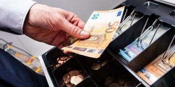 Una persona sostiene euros en efectivo sobre caja registradosra.