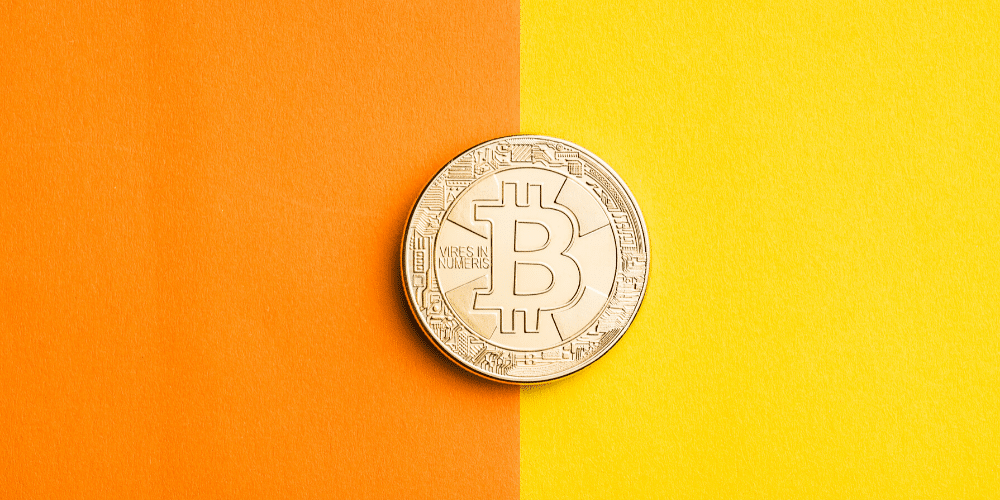 Un bitcoin posado en un papel bicolor. Fuente: jirkaejc/ Envato Elements.