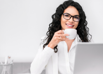 Una mujer toma café frente a un escritorio de trabajo. Fuente: Prostock-studio/ Envato Elements.