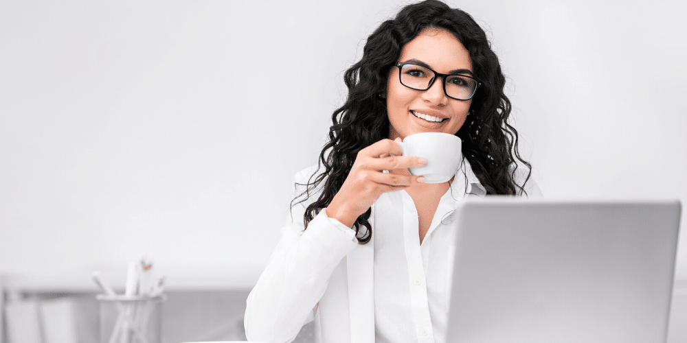 Una mujer toma café frente a un escritorio de trabajo. Fuente: Prostock-studio/ Envato Elements.