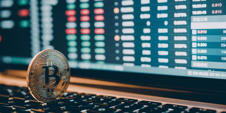 Un bitcoin en una computadora, tras de él órdenes de compra. Fuente: Panxunbin/ Envato Elements.