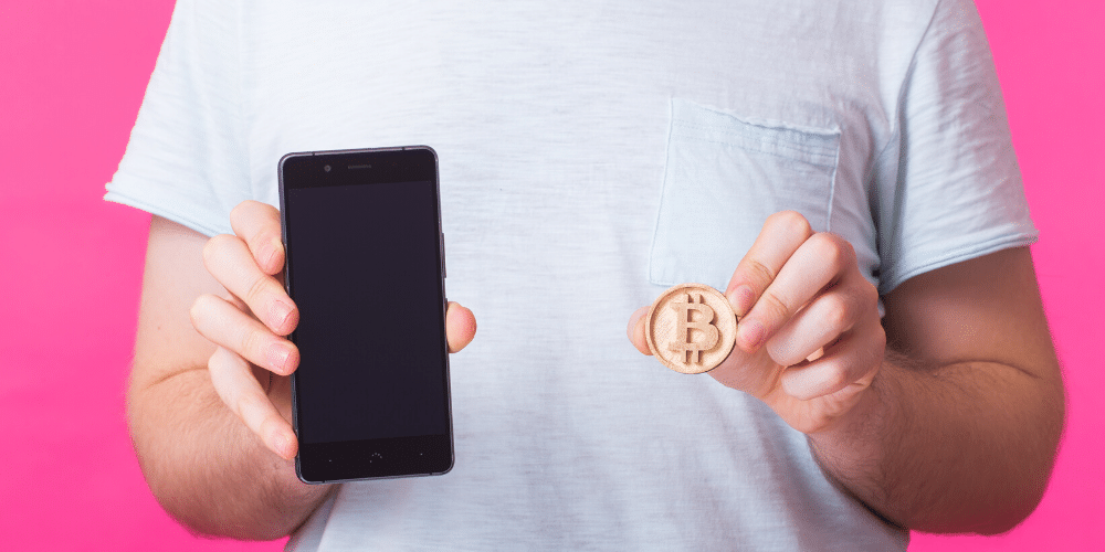 Un hombre enseña su bitcoin y teléfono celular. Fuente: Satura_/ Envato Elements.