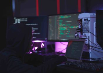 Portrait of unrecognizable hacker using computer equipment with programming code on screens in dark room, cyber security concept, copy space. Fuente: