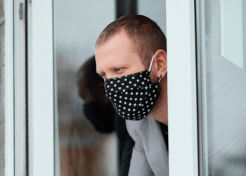 Un hombre mira por la ventana con mascarilla. Fuente: bondarillia/ Envato Elements.