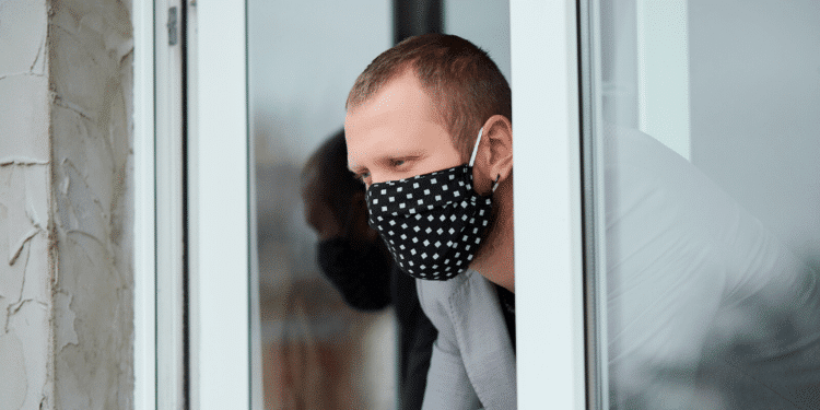Un hombre mira por la ventana con mascarilla. Fuente: bondarillia/ Envato Elements.