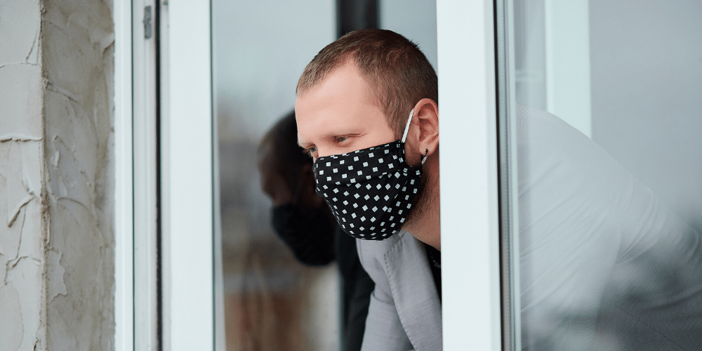 Un hombre mira por la ventana con mascarilla. Fuente: bondarillia/ Envato Elements.