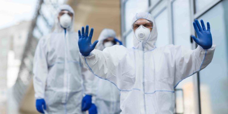 Hombre vistiendo traje protector contra el coronavirus haciendo gestos para detener a las personas. Fuente: Prostock-studio/ Envato Elements