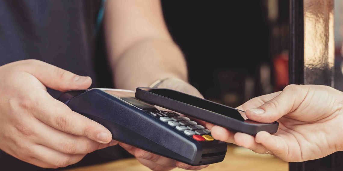 Persona realizando un pago por medio de su smartphone usando la tecnología NFC en una cafetería al aire libre. Fuente: KonstantinKolosov/ elements.envato.com