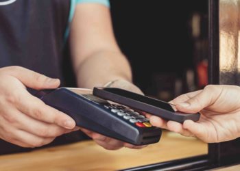 Persona realizando un pago por medio de su smartphone usando la tecnología NFC en una cafetería al aire libre. Fuente: KonstantinKolosov/ elements.envato.com