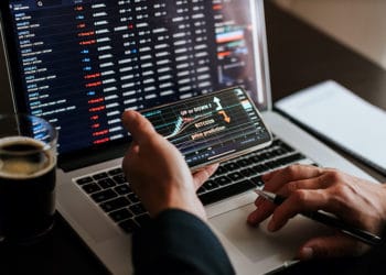 Hombre evaluando el mercado de las criptomonedas en la pantalla de un teléfono y en la computadora. Fuente: avanti_photo /   elements.envato.com