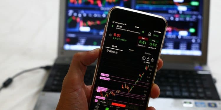 Mano sosteniendo un dispositivo con gráficas de mercado frente a una computadora. Fuente: Sergei Tokmakov, Esq. / Pixabay