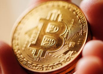 Hombre sosteniendo de cerca moneda dorada de Bitcoin. Fuente: stevanovicigor / elements.envato.com