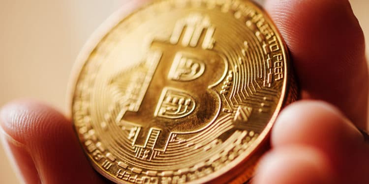 Hombre sosteniendo de cerca moneda dorada de Bitcoin. Fuente: stevanovicigor / elements.envato.com