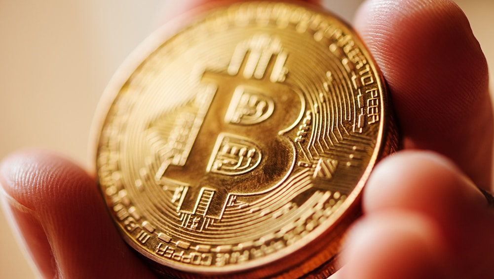 Hombre sosteniendo de cerca moneda dorada de Bitcoin. Fuente: stevanovicigor / elements.envato.com