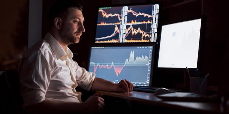 Trader en habitación oscura con gráficos de mercados en pantallas. Fuente: mstandret / elements.envato.com