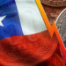 Bandera de Chile sobre monedas de peso junto a flecha descendiente y monedas de bitcoin. Composición por CriptoNoticias. LightFieldStudios / elements.envato.com; Maciejbledowski / elements.envato.com; wirestock / freepik.com; twenty20photos / elements.envato.com.