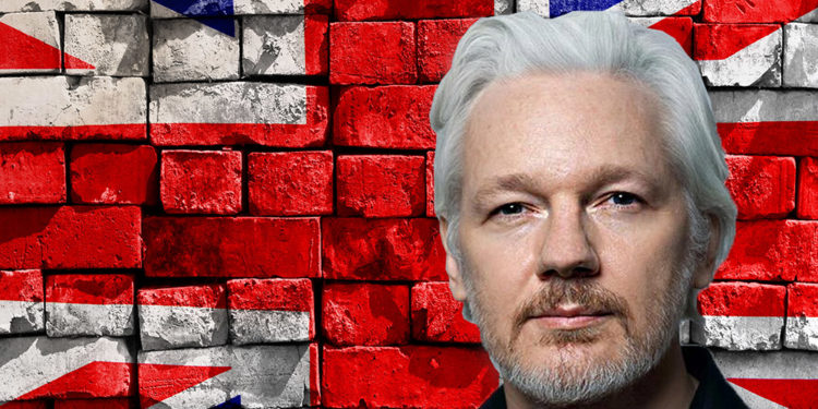Julian Assange frente a pared de ladrillos con bandera de Reino Unido pintada. Composición por CriptoNoticias.lawyers Weekly / lawyersweekly.com; twenty20photos / elements.envato.com.