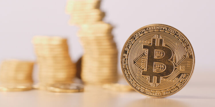 Moneda de bitcoin frente a monedas apiladas. Composición por CriptoNoticias. leungchopan / elements.envato.com