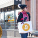 Mujer con bolsa de compras con logo de bitcoin con tienda de BitBase y moneda de Bitcoin en el fondo. Composición por CriptoNoticias. Bitcoin / bitcoin.org; LightFieldStudios / elements.envato.com; BitBase / bitbase.es; twenty20photos / elements.envato.com.