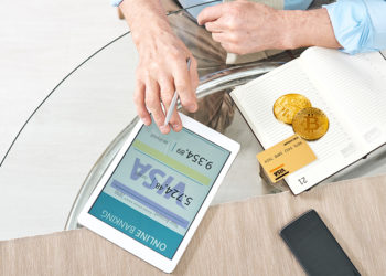 Hombre revisa cuenta bancaria con tarjeta y monedas de bitcoin sobre mesa con logo de Visa. Composición por CriptoNoticias. Photology75 / elements.envato.com; Visa / wikipedia.org; Pressmaster / elements.envato.com.