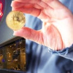 Mano de hombre con criptomoneda bitcoin afuera de tienda Rakuten.