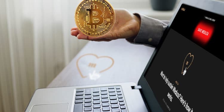Escritorio con logo de Meduza y laptop con home de meduza.oi y mano sosteniendo bitcoin.