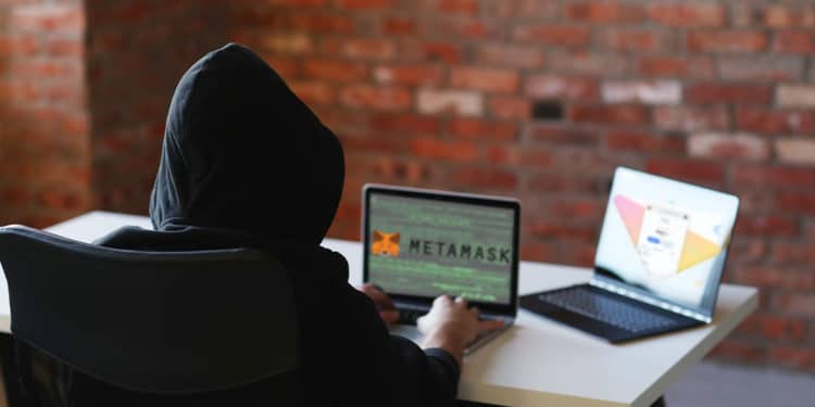 Hacker con dos pantallas, en una logo de Metamask y en otra mockup de la app de Metamask.