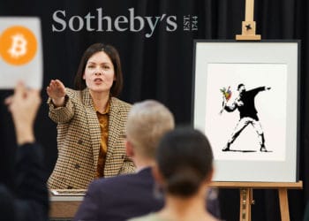 Subasta de obra de Banksy, persona ofertando en bitcoin y logo de Sotheby's al fondo.