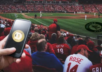 Estadio de beisbol de los Atléticos de Oakland y mano sosteniendo teléfono con dogecoin.