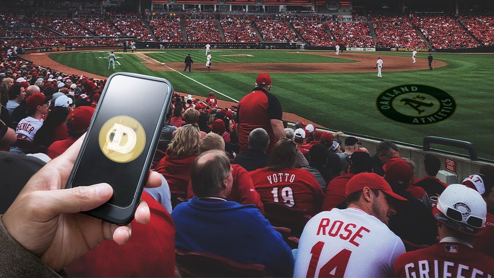 Estadio de beisbol de los Atléticos de Oakland y mano sosteniendo teléfono con dogecoin.