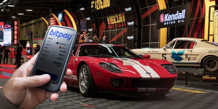 Subasta de auto con mano sosteniendo teléfono que tiene bitpay en pantalla.