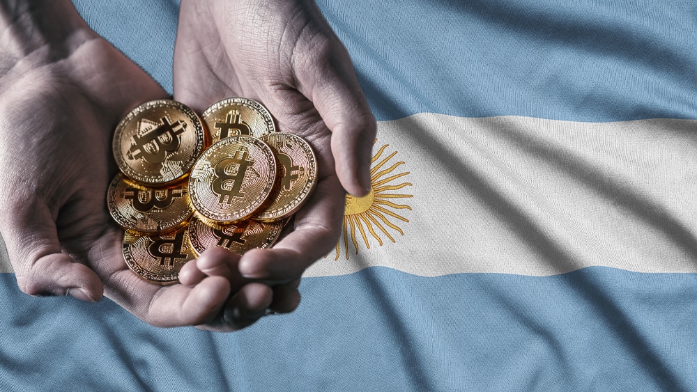 Bandera de Argentina y y mano sosteniendo bitcoins.