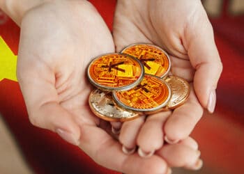 Manos sosteniendo monedas físicas de yuan. En el fondo, bandera china.