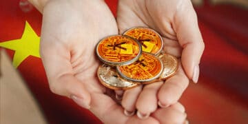 Manos sosteniendo monedas físicas de yuan. En el fondo, bandera china.
