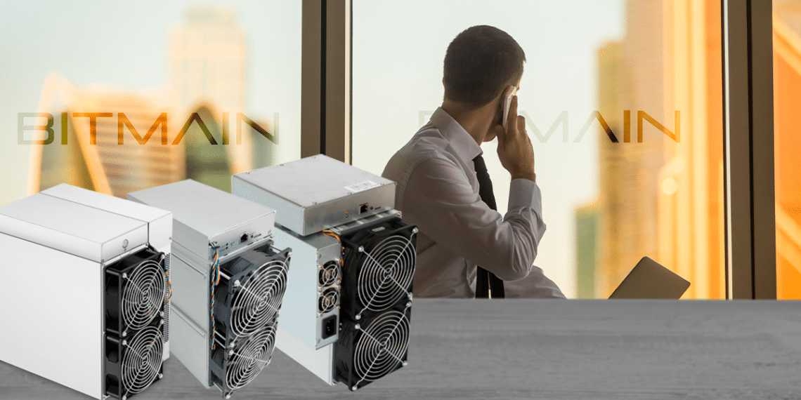 Persona en oficina con logo de Bitmain y varios Antminer sobre mesa.