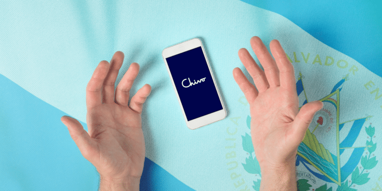 Manos reclamando a un teléfono con logo de Chivo Wallet y bandera de El Salvador de fondo.