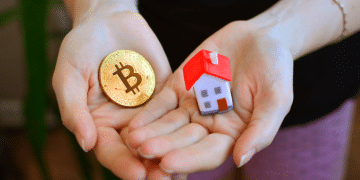 Unas manos sostienen una casa en miniatura y una moneda de bitcoin.