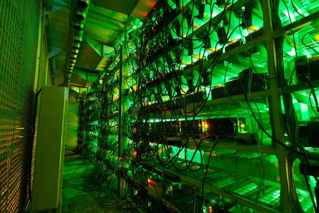 Una hilera de equipos ASIC iluminados con luz verde - Qué es una granja de minería de Bitcoin - CriptoNoticias