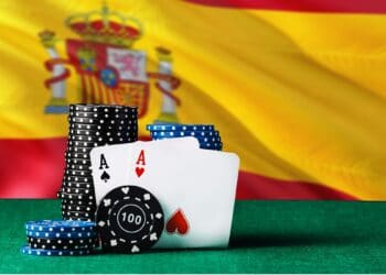 Dos ases de poker sostenidos por fichas de apuestas frente a la bandera de España.