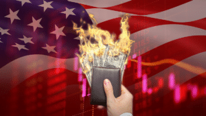 La mano de una persona sosteniendo una cartera con dólares en llamas frente una bandera de Estados Unidos y un gráfico de precios en rojo.