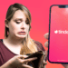 Persona preocupada por tener la billetera vacía y teléfono con logo de Tinder.