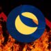 Logo del cripto LUNA sobre fuego y una flecha roja fracturada descendiente detrás