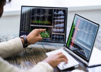 Un hombre frente a dos pantallas de computador con gráficos de precios