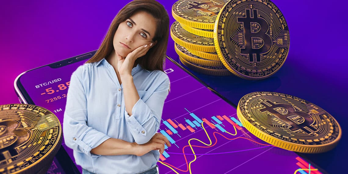 mujer con gesto de duda en frente de moneda de bitcoin con gráfico de precio en pantalla de teléfono