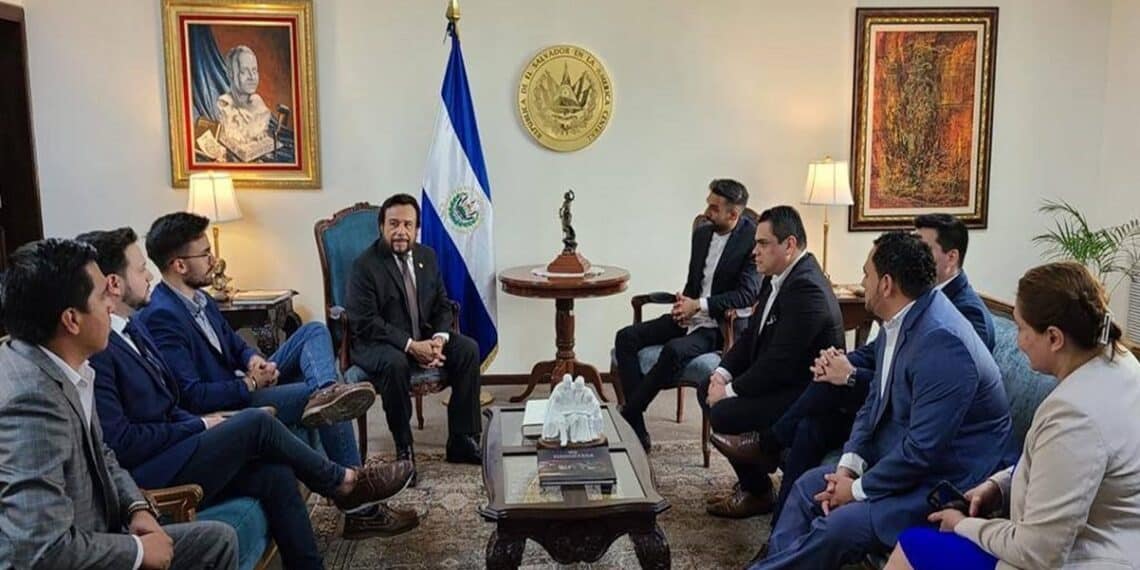 Varias personas reunidas en una sala con la bandera de El Salvador al fondo.