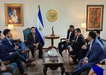 Varias personas reunidas en una sala con la bandera de El Salvador al fondo.