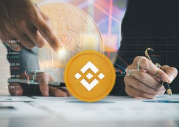 moneda de Binance en frende de gráficos y analistas de mercado con moneda de bitcoin difuminada en el fondo