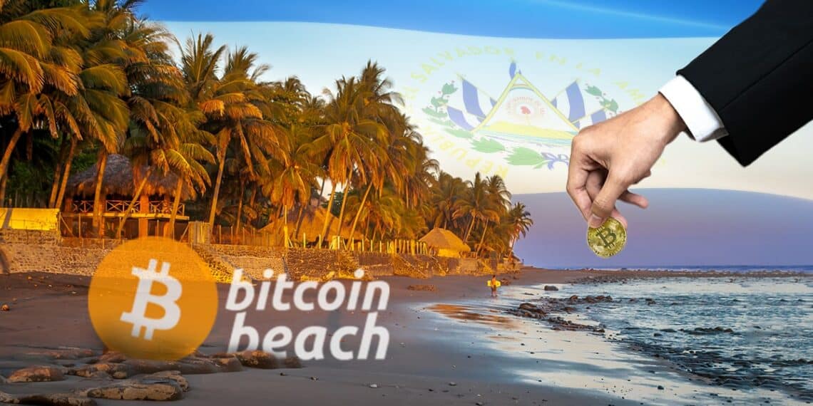 mano depositando moneda de bitcoin en playa con logo de Bitcoin Beach y bandera de El Salvador en el fondo